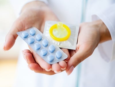 Een dokter houdt potentiepillen en een condoom in zijn handen